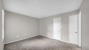 A room with white walls and carpeted floor with three doors.